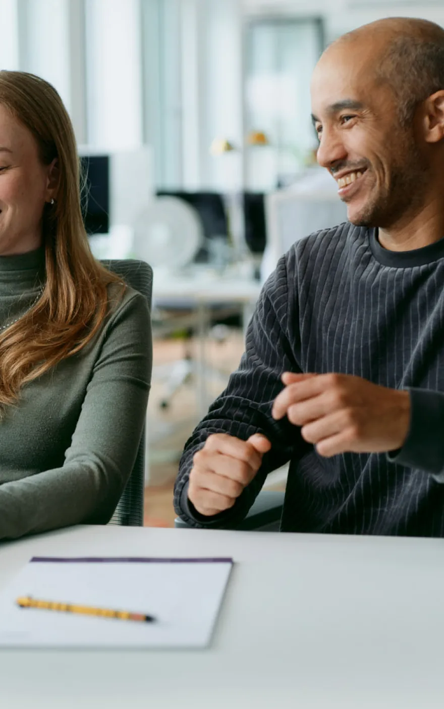 Zwei Kolleg:innen lachen gemeinsam am Besprechungstisch