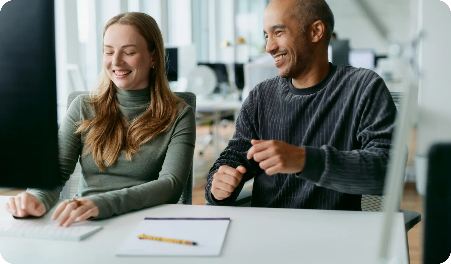 Zwei Kolleg:innen lachen gemeinsam am Schreibtisch